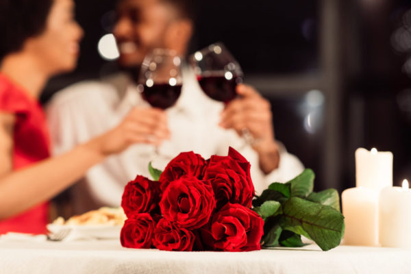 Valentine's Romantic Date. Red Roses Lying On Table, Unrecognizable Spouses Drinking Wine In Restaurant. Selective Focus, Cropped