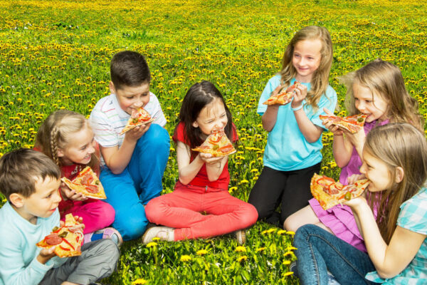 Group of children eating pizza outdoors