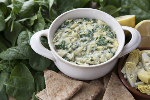 Bowl of vegan spinach artichoke dip with pita and ingredients.