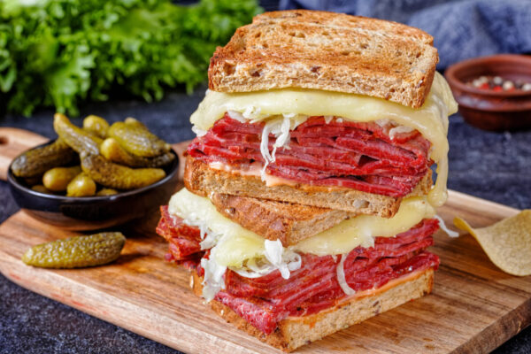 reuben sandwich with rye bread thinly sliced corned beef, sauerkraut, thousand islands dressing and melted cheese on board with pickles and  potato chips, close-up